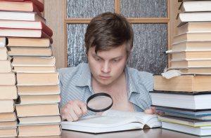 Young crazy student with loupe  between books searching something