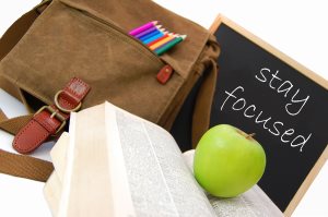 Satchel, book and apple with words "stay focused" on chalkboard