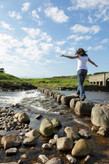 Young girl runs across stepping stones to cross a stream