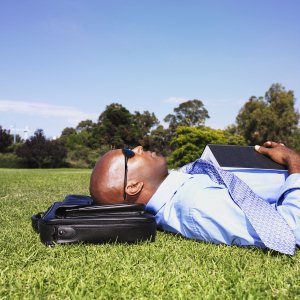 Businessman lying in grass with book