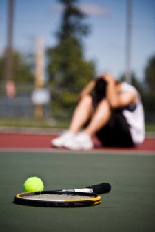 A sad male tennis player sitting down in disappointment after defeat