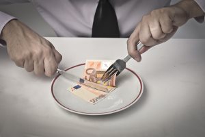 Businessman's hands cutting a banknote in a dish with fork and knife