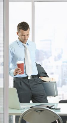 Businessman leaving office, holding suitcase and coffee cup in hand