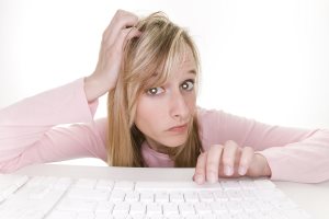 Confused teenage girl using computer, white indoor studio, looking into monitor