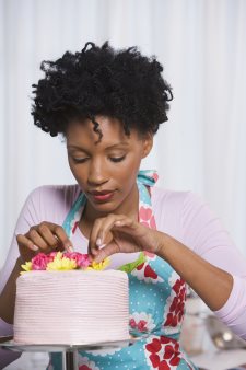 Young Black woman putting flowers on cake