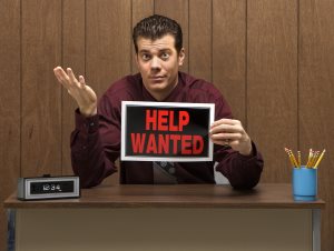 businessman sitting at desk holding help wanted sign