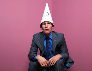 Businessman Sat In Corner Wearing Dunce Hat