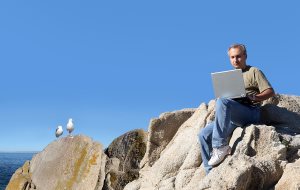 Man sitting on the rock and working on his laptop