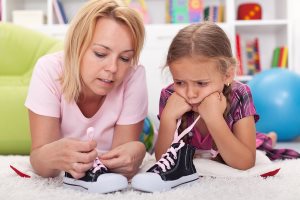 Mother teaching little unhappy girl to tie her shoes 