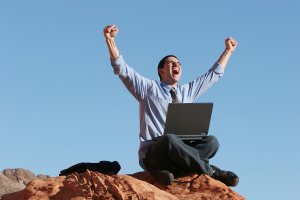 Young businessman sitting on cliff working on his laptop