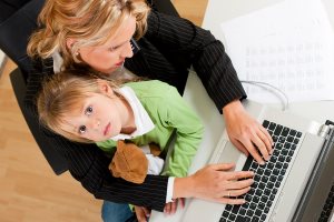 telecommuter Businesswoman and mother working on laptop while her daughter looks to the viewer