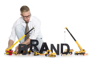 Focused businessman building the word brand along with construction machines