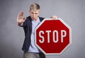 Serious man showing stop gesture with hand as warning while holding stop sign 