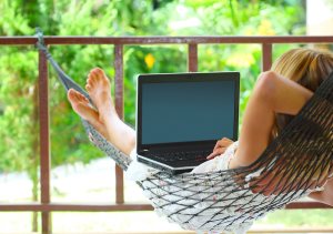 Young woman sitting in a hammock in a garden with laptop