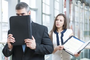 Businessman hides from coworker behind folder