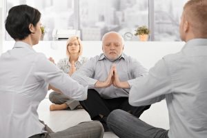 Businesspeople exercising yoga in office with eyes closed
