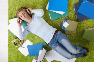 Woman lying on floor with closed eyes listening to music in headphones, surrounded with papers