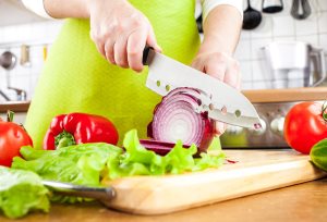 Woman's hands cutting bulb onion, behind fresh vegetables