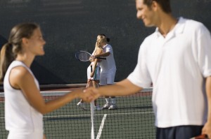 Tennis players shaking hands at net with teammates hugging in background