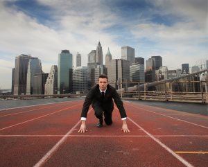 Businessman kneeling on the starting grid of a running track with cityscape on the background