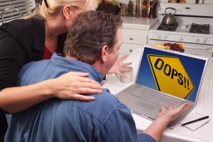 Couple In Kitchen Using Laptop with Yellow Oops Road Sign on the Screen