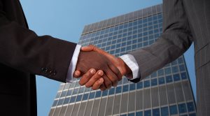 two business hands performing a handshake with a corporate building