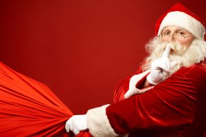 Santa Claus with huge red sack keeping forefinger by his mouth