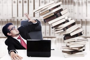 Scared businessman with stack of books about to collapse