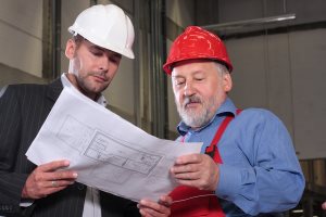 businessmen and older worker wearing hardhats looking at a set of blueprints 