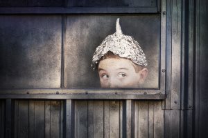 Boy in a tin foil hat peeking out of a window