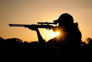 Silhouette of a young man shooting with a long rifle