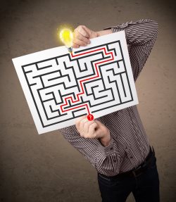 businessman holding a paper with a labyrinth on it in front of his head