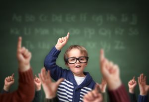 School child with hand raised in the classroom in front of a blackboard