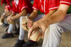 baseball team mates sitting in dugout with player holding a ball
