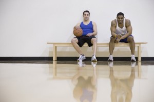 Two men sitting on sidelines of basketball court