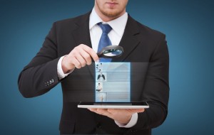 businessman holding magnifying glass over tablet 