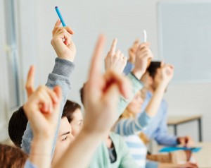Many students raising their hands in class